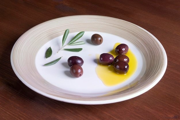 Olive oil and olives on a plate on wooden surface with some olive branches