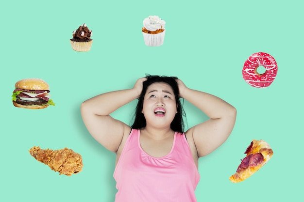 Portrait of an obese woman looks sad and screaming surrounded by unhealthy food