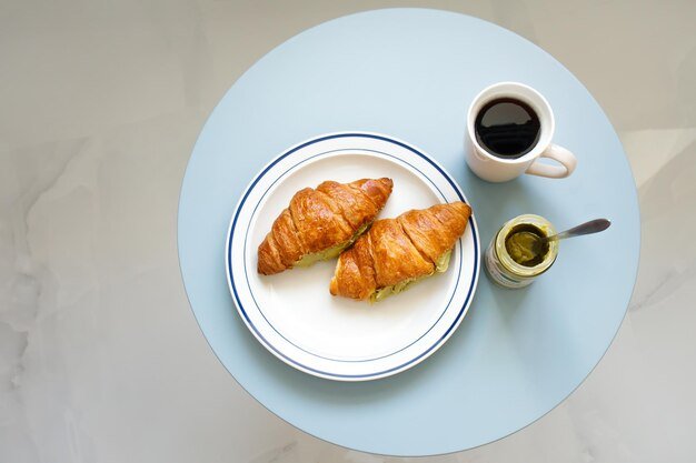 Two croissants filled with pistachio cream paste with black coffee on blue table top view