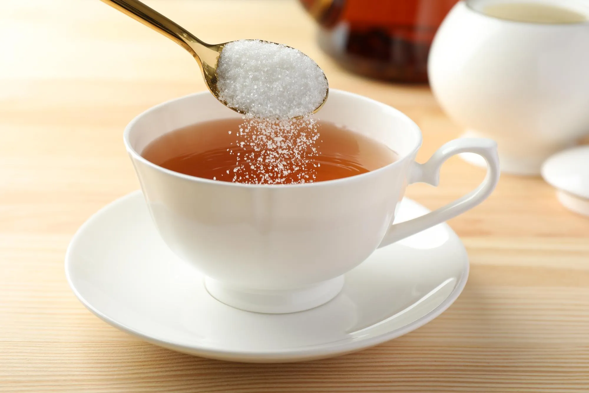 Adding sugar into cup of tea at wooden table closeup
