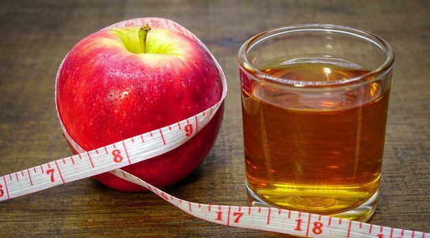 Apple cider vinegar in a glass with apples and a measuring tape on a wooden background