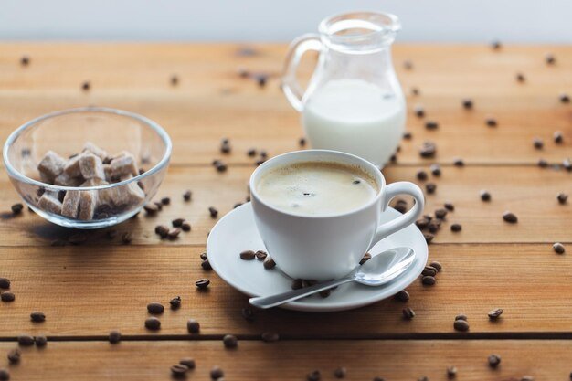 caffeine, objects and drinks concept - close up coffee cup and grains on wooden table