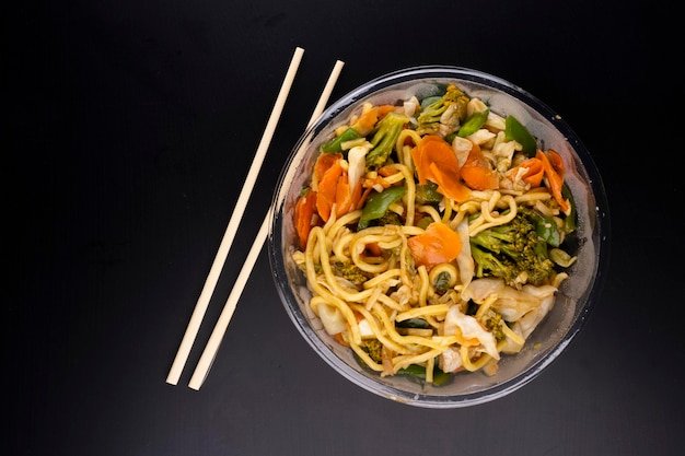 Chinese food delivery vegetarian yakisoba bowl top view black background with chopsticks