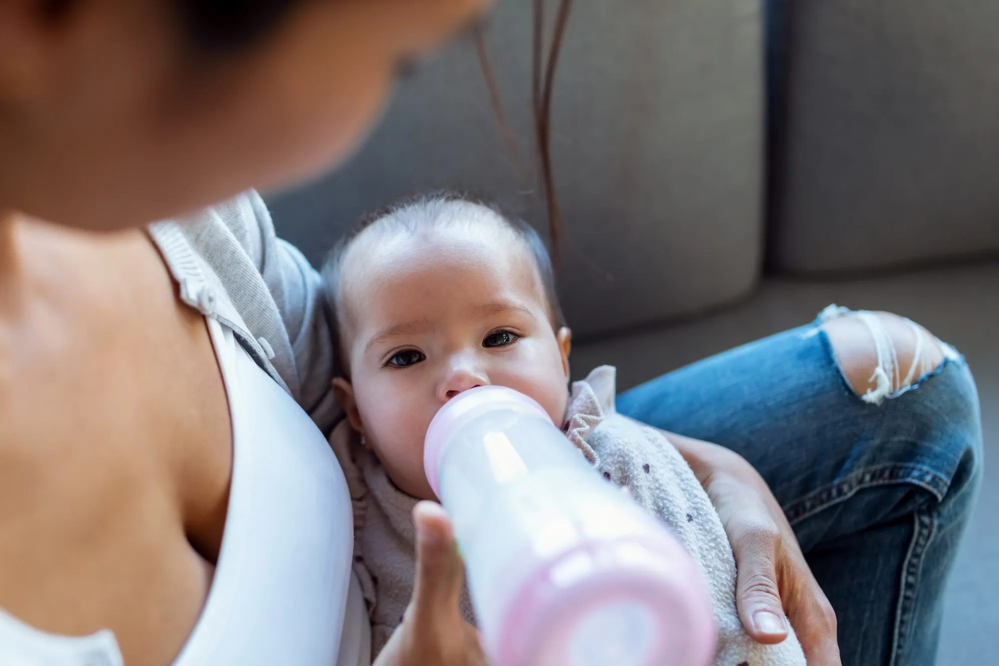 Close-up of mother feeding her baby daughter with feeding bottle while sitting on sofa at home.
