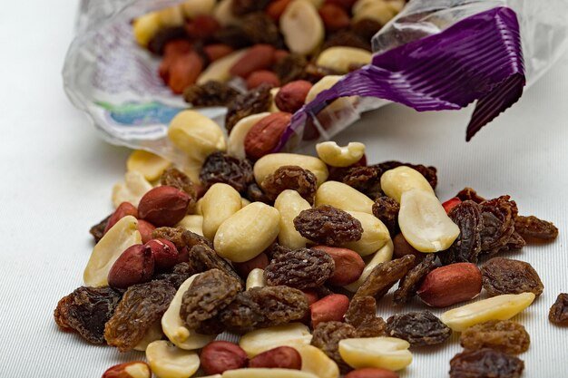 Close up of nuts and dried fruit spilling out of a packet isolated against a plain background