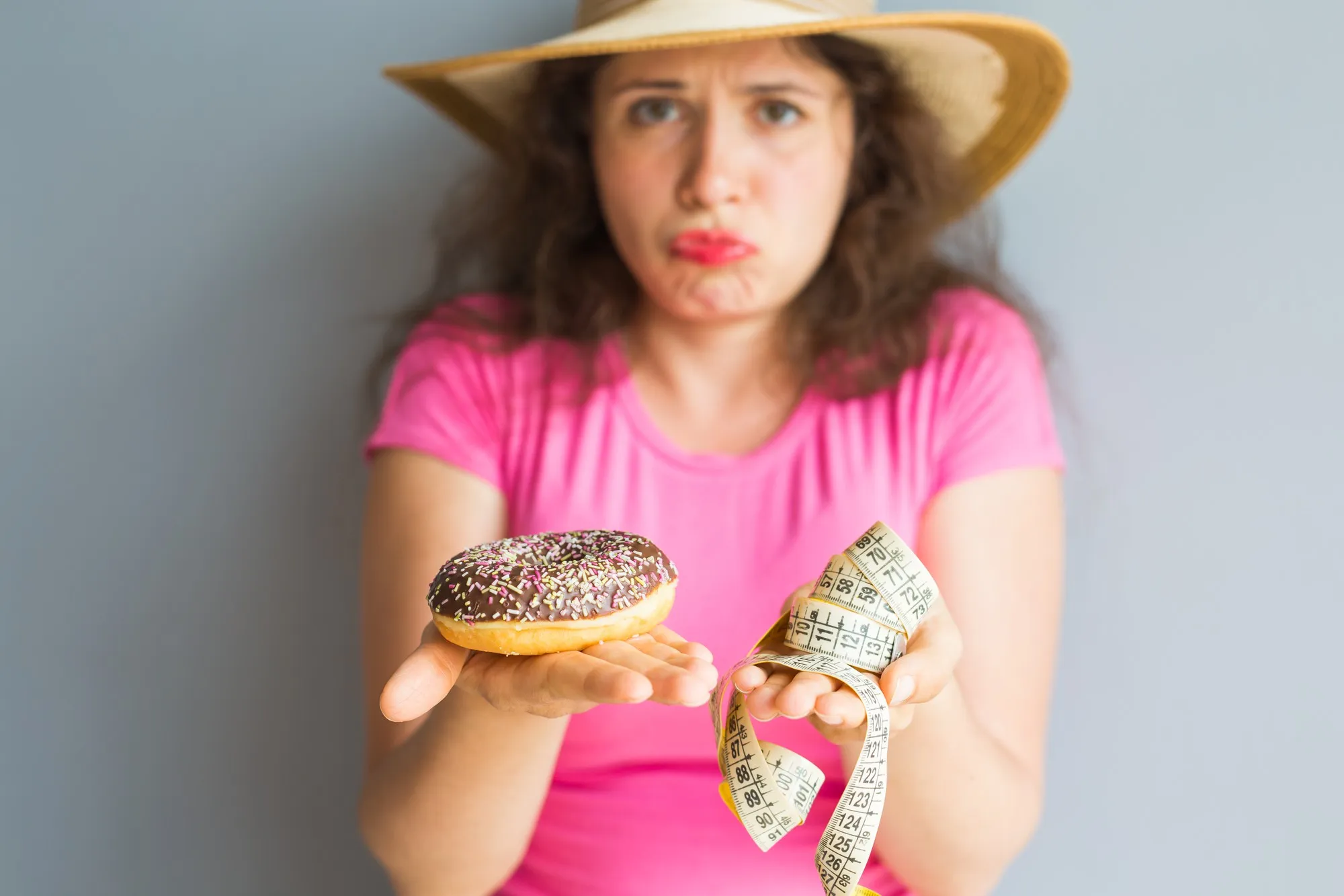 Confused young woman holding a donut and a measuring tape. Concept of Sweets, Unhealthy Junk Food and obesity.