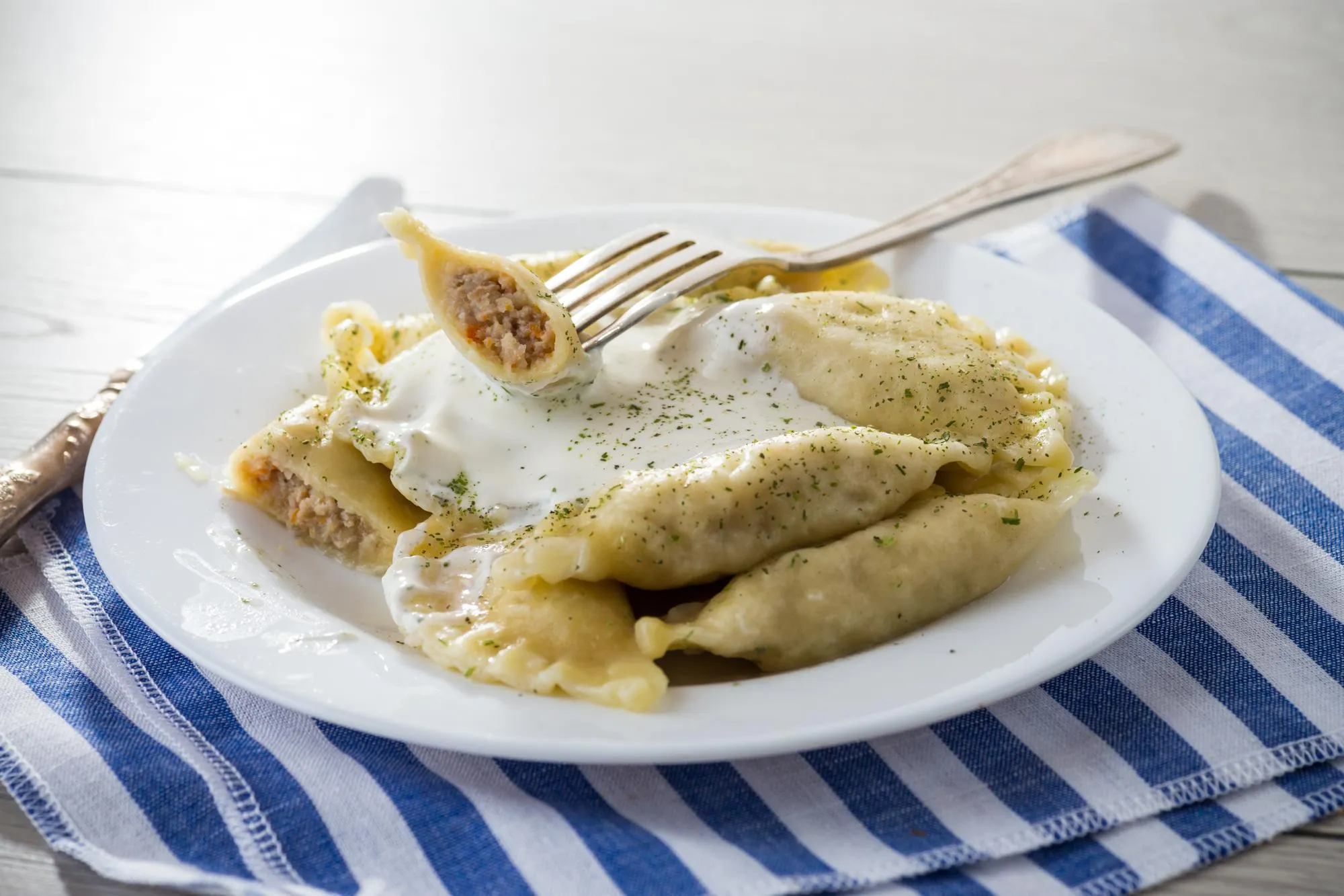 cooked dumplings with meat spices and sour cream in a plate on a light wooden table Ukrainian food
