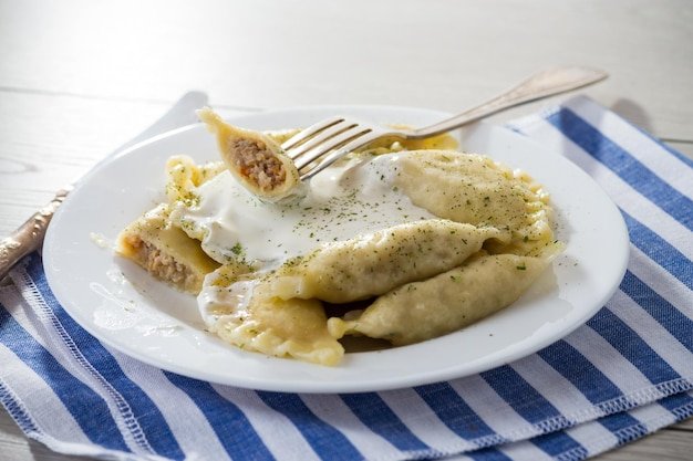 cooked dumplings with meat spices and sour cream in a plate on a light wooden table Ukrainian food