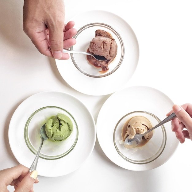 Cropped hand of people eating ice cream on table