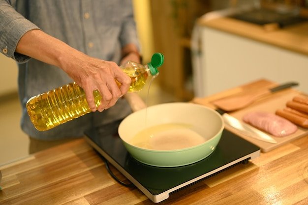 Cropped shot man pouring oil into a frying pan during meal preparation