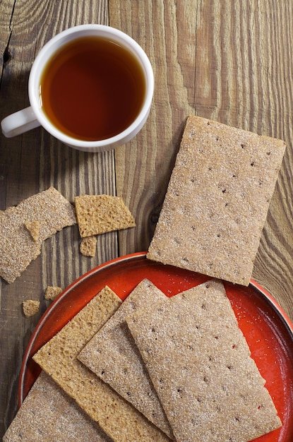 Cup of tea and crisp bread in red plate on the wooden table, top view. Diet food