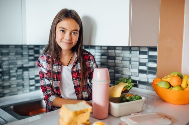 Cute young girl smiles and holds her healthy sandwich over her lunch box
