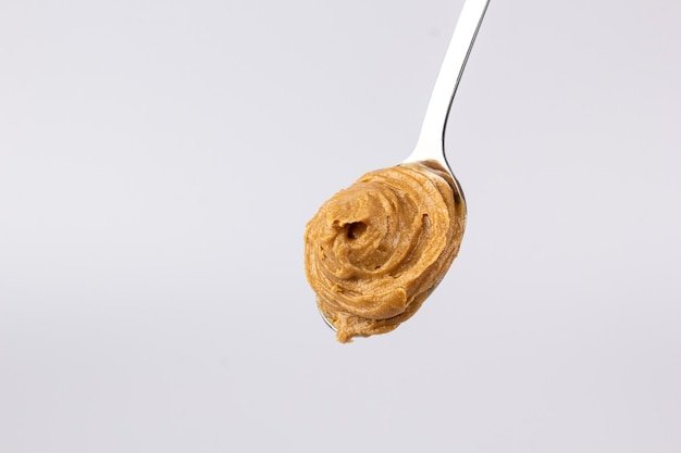 Delicious creamy peanut butter is laid out in a beautiful slide in a spoon on a white background Tasty breakfast Healthy food concept