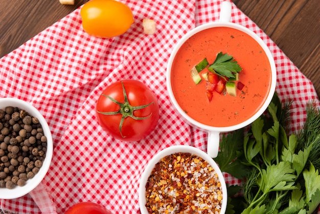 Delicious tomato cream soup on a wooden background. Top view. With vegetables, bell peppers, herbs and tomatoes.