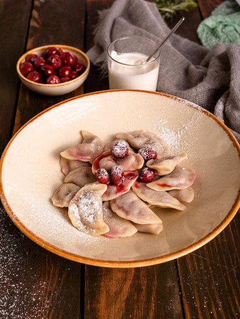 Dumplings with cherries and sour cream in a plate on a wooden table