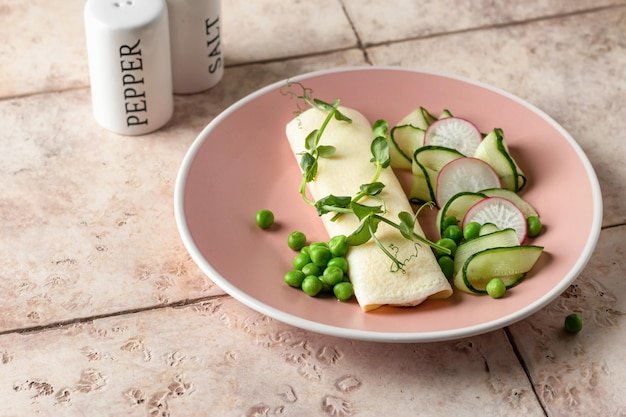 French vegetarian omelet roll filled with cream cheese with green peas microgreens and cucumber radish salad for breakfast on pink tile background Copy space