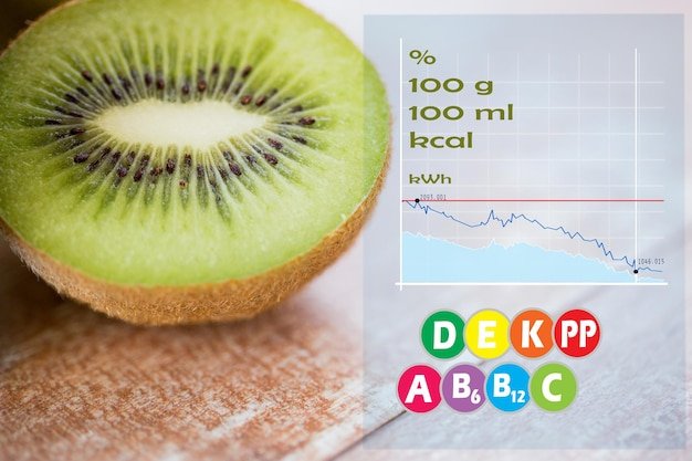 fruits, diet, food and objects concept - close up of ripe kiwi slice on table with calories and vitamin chart