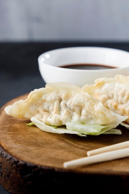 Gyozas served in black plate on wooden log, with chopsticks and black background