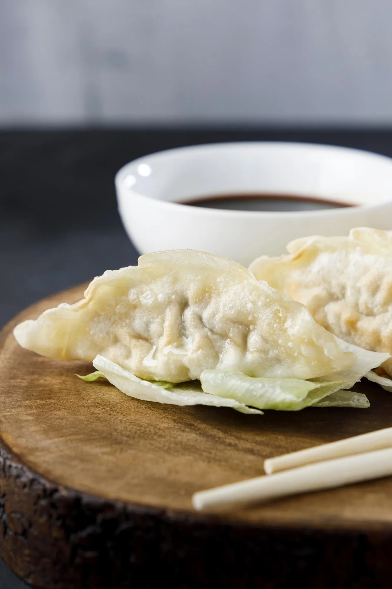 Gyozas served in black plate on wooden log, with chopsticks and black background