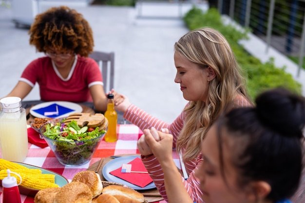Happy diverse group of friends praying and having dinner at balcony with flags of usa