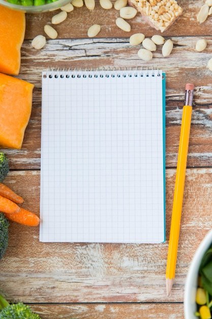 healthy eating, vegetarian food, advertisement and culinary concept - close up of ripe vegetables and notebook with pencil on wooden table