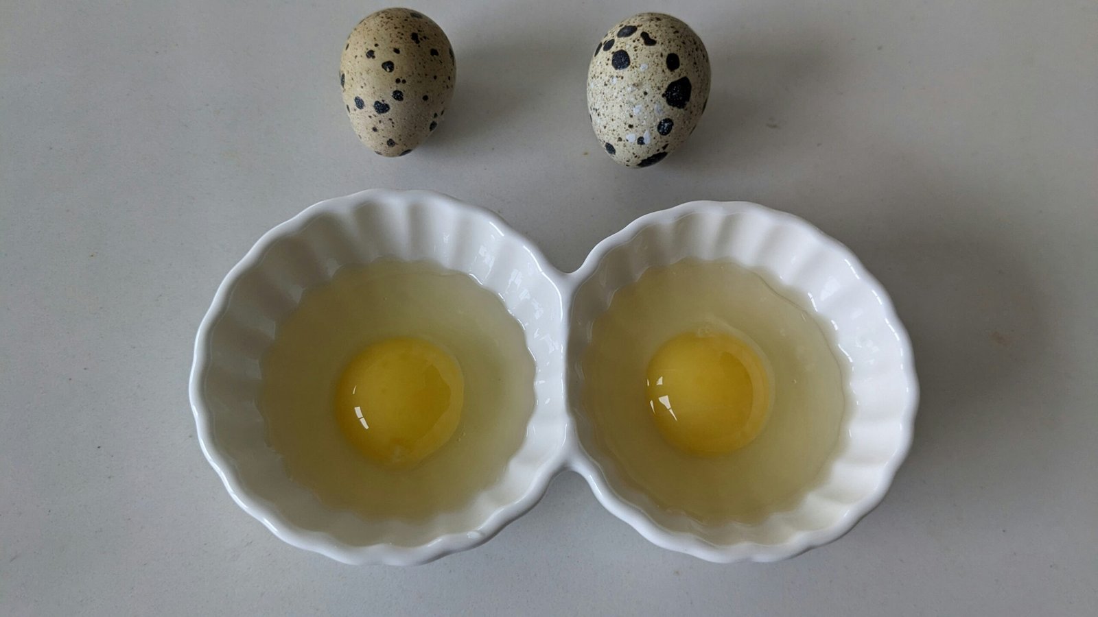 A couple of eggs sitting in a bowl next to two quails