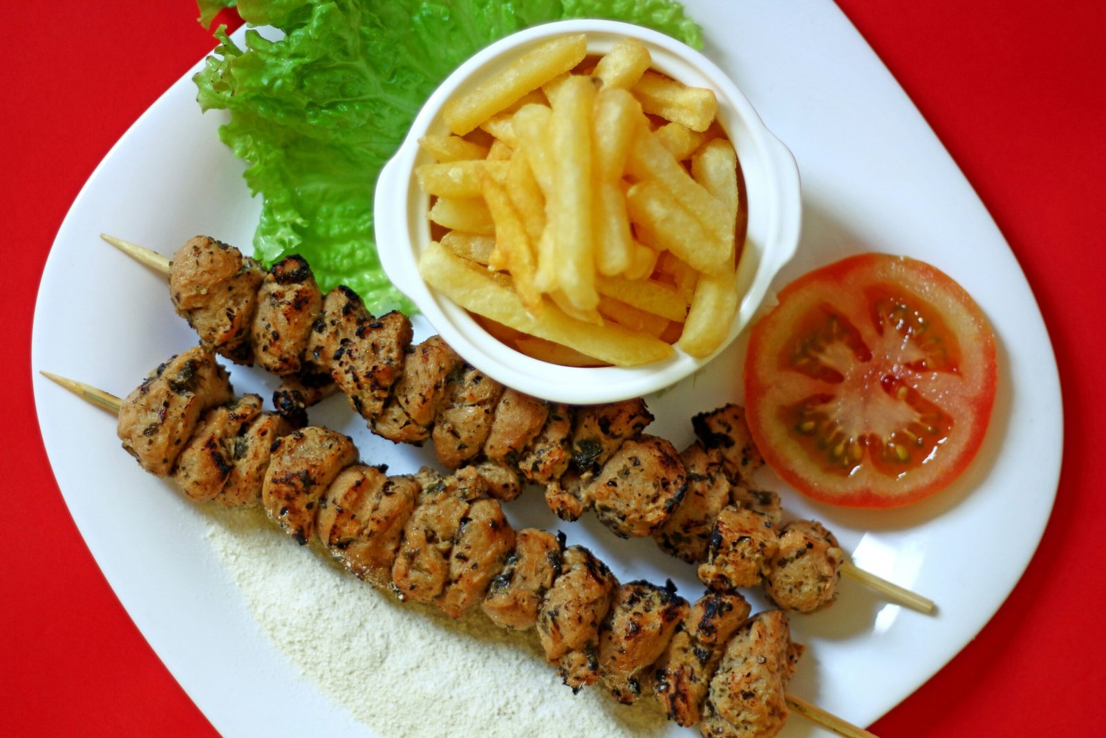 A white plate topped with kebabs and french fries