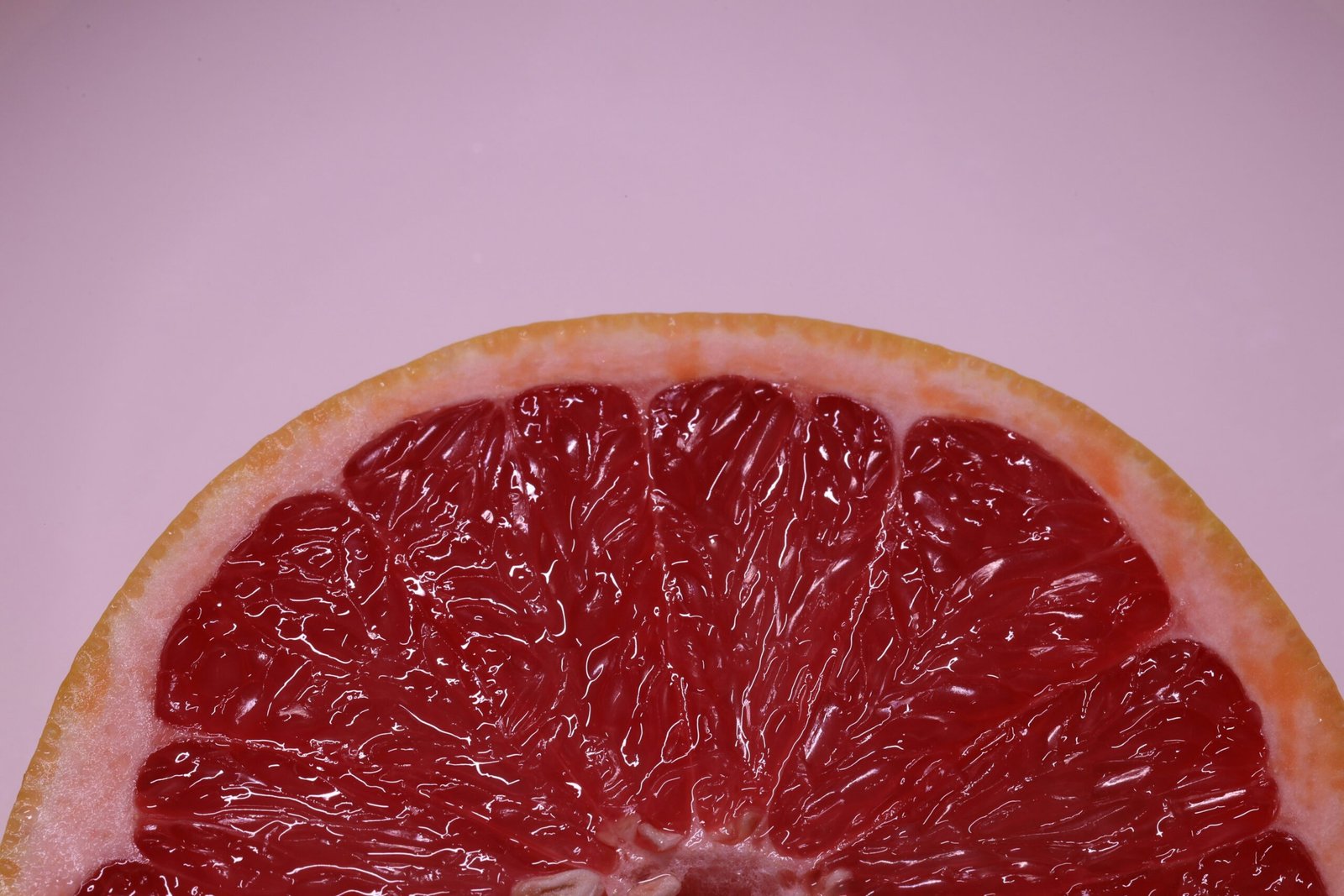 a grapefruit cut in half on a pink background
