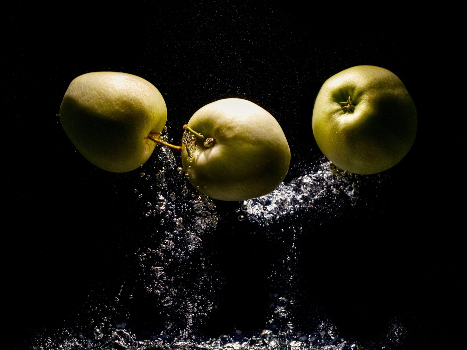 two green apples falling into water on a black background