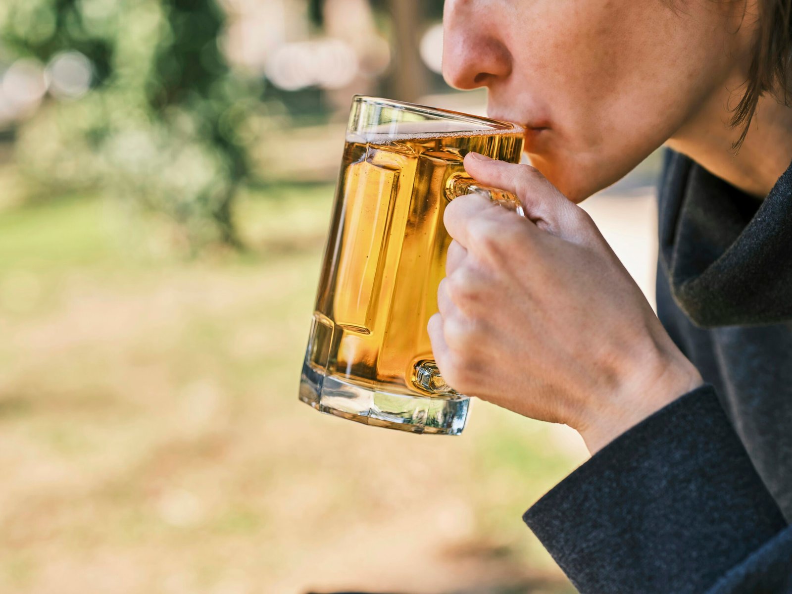 a woman drinking a glass of beer in a park