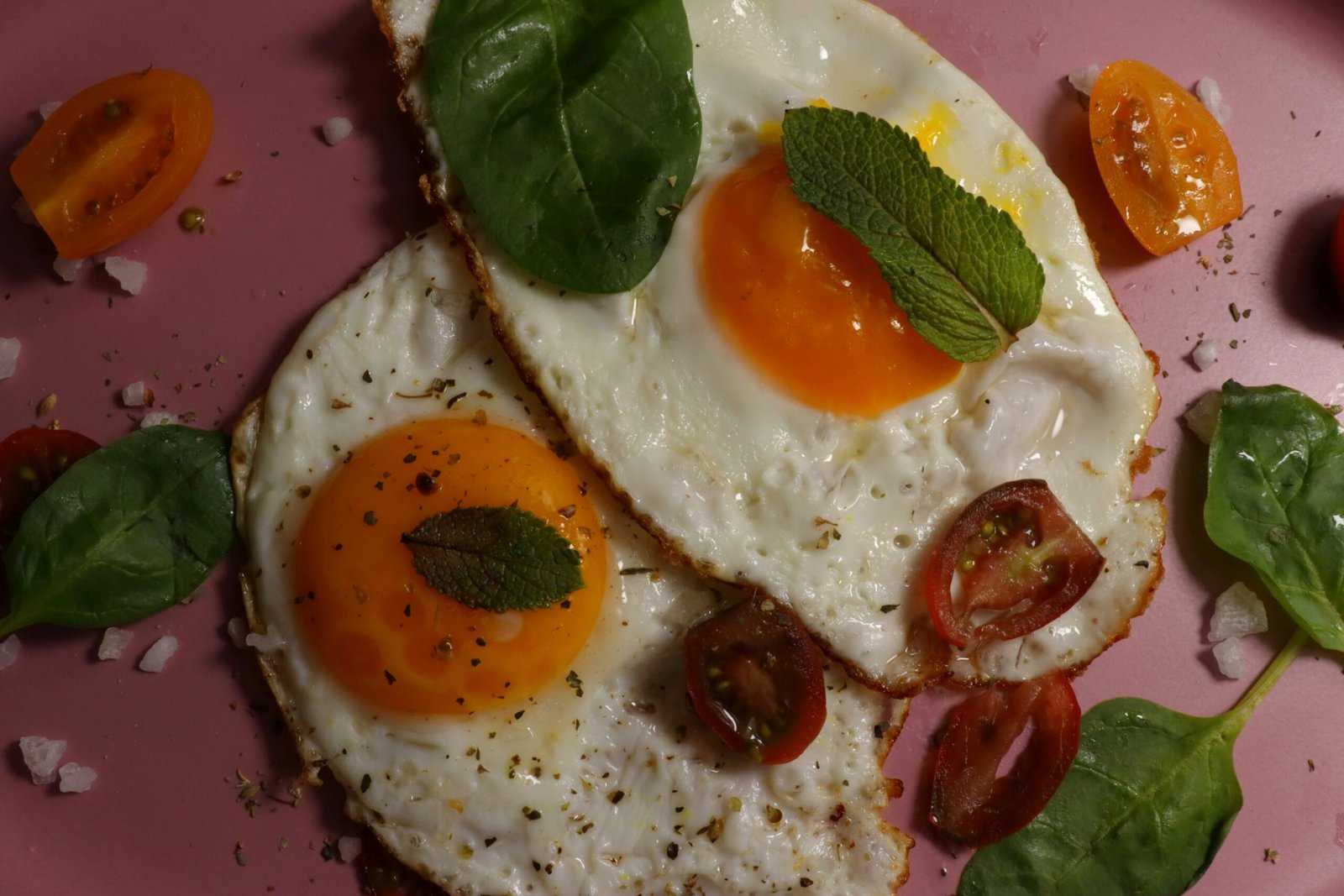 Fried eggs and tomatoes on a pink plate.