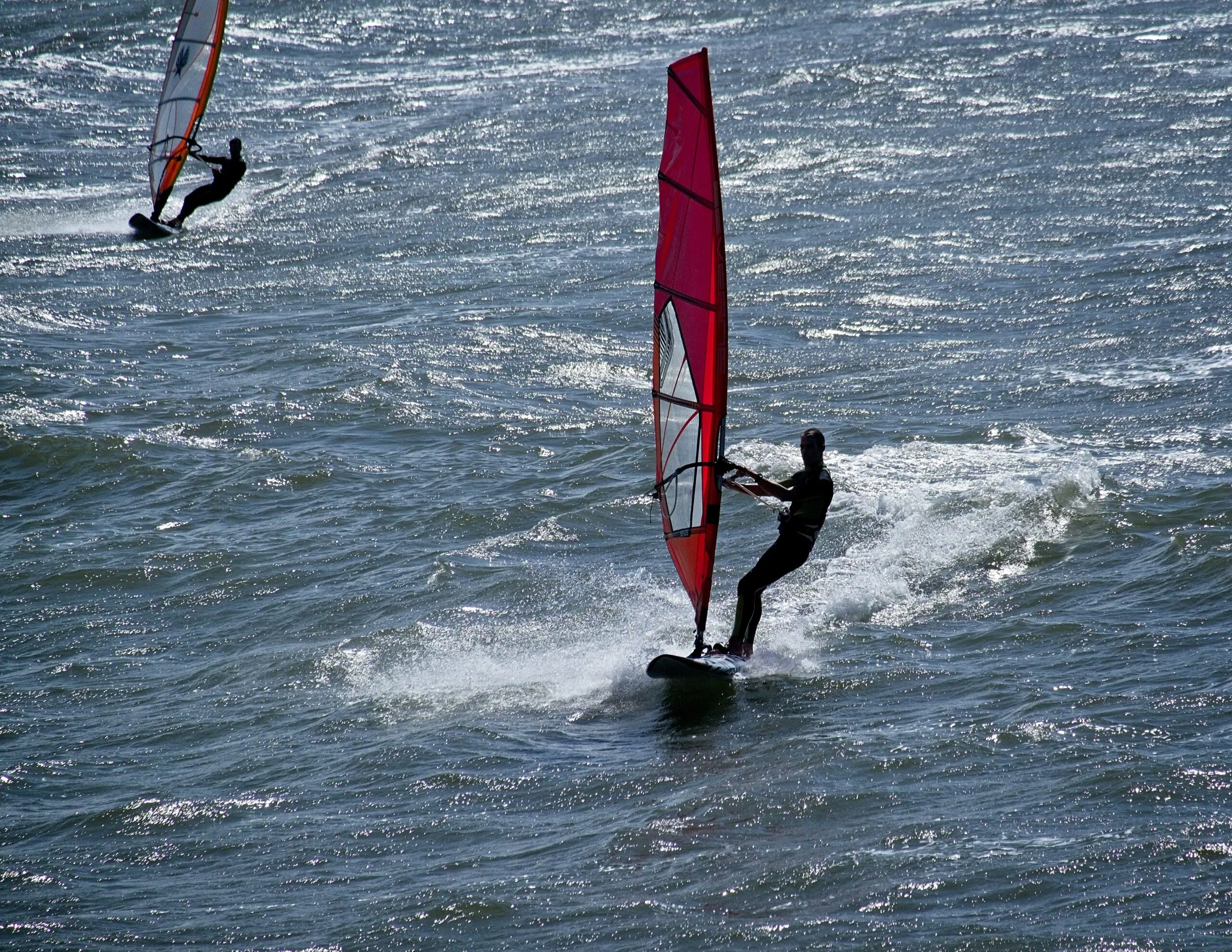 Two people windsurfing on a choppy sea.