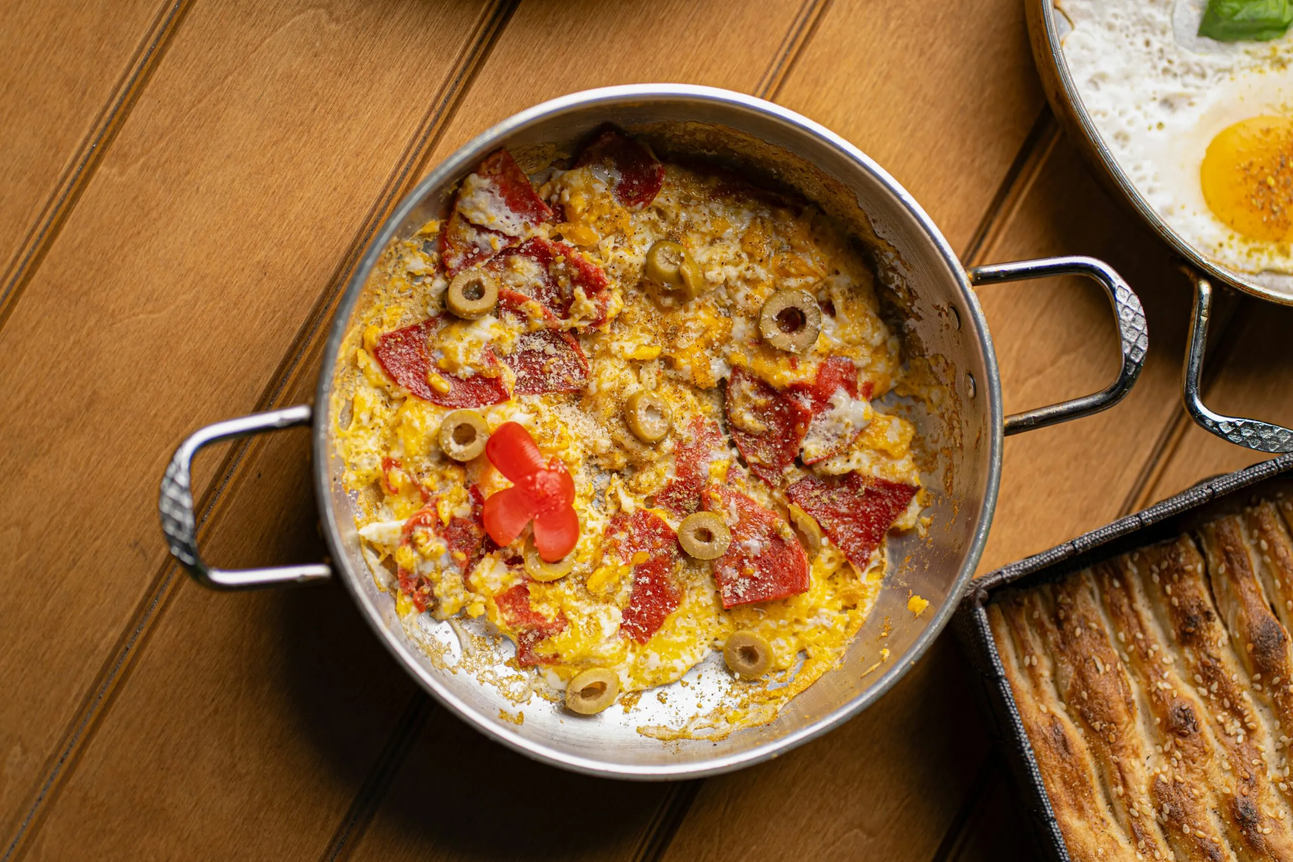Scrambled eggs with tomatoes, olives, and meat in pan.