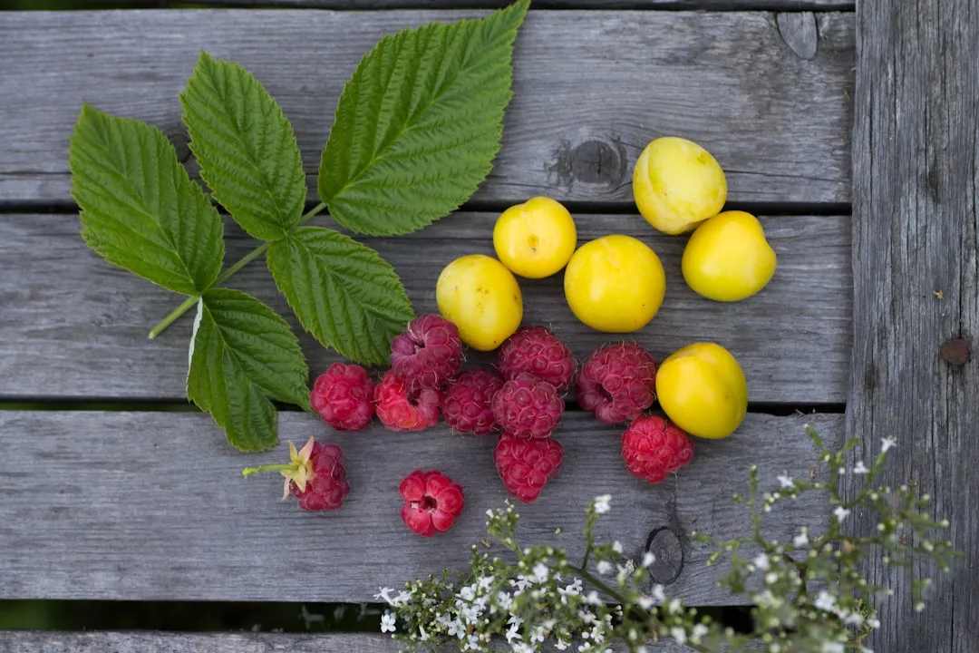 Raspberries and yellow plums with leaves on wood
