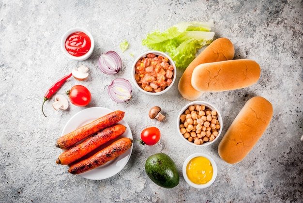 Ingredients for different homemade Vegan Carrot Hot Dogs, with fried onion, avocado, chili, mushrooms, tomatoes and beans, grey stone copyspace top view