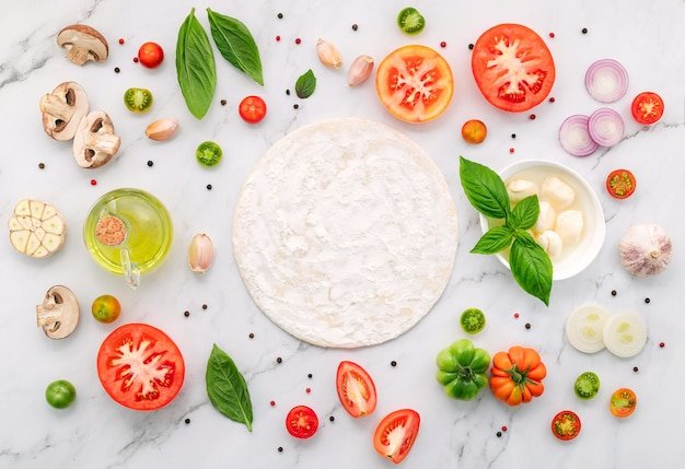 The ingredients for homemade pizza set up on white marble background.