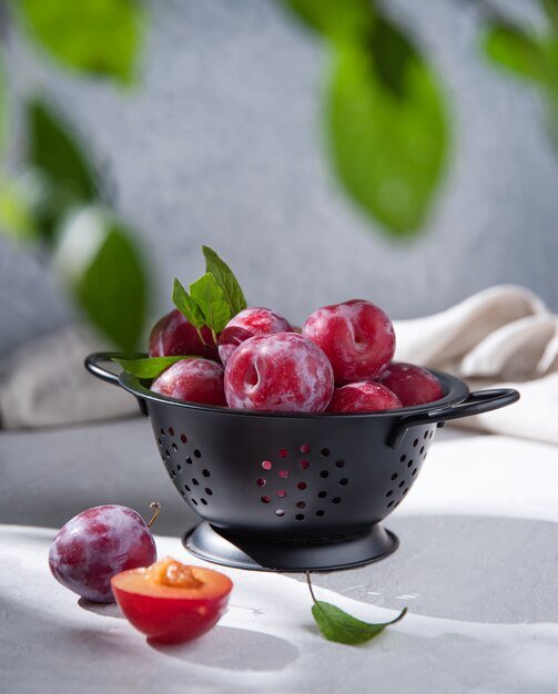 Juicy ripe purple plums in a black bowl on a light table