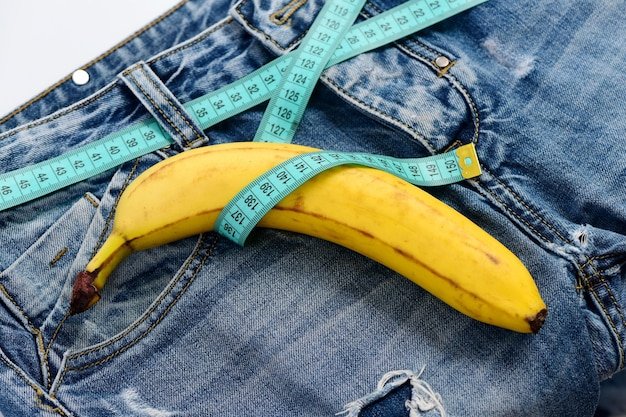 Mens denim pants with banana imitating male genitals Kinky fruit on denim fabric close up Health and male sexuality concept Blue jeans with measure tape instead of belt on white background