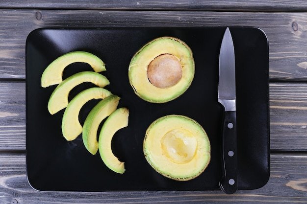Plate with sliced avocado on wooden background top view