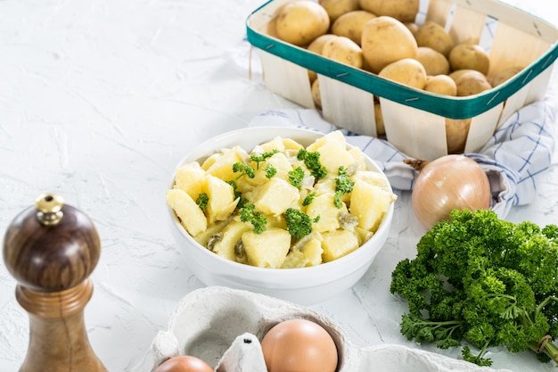 Potato salad and potatoes and herbs on white concrete countertop