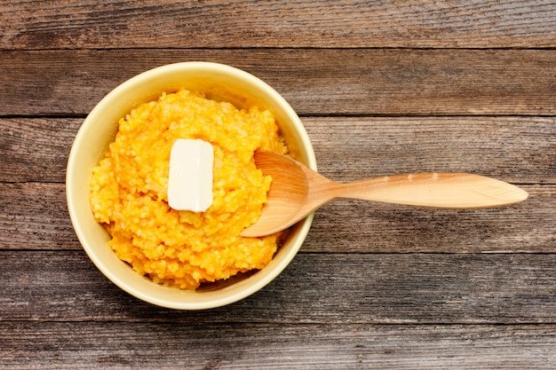 Rice porridge from pumpkin with milk and butter, and wooden spoon on wooden retro grunge background top view close-up