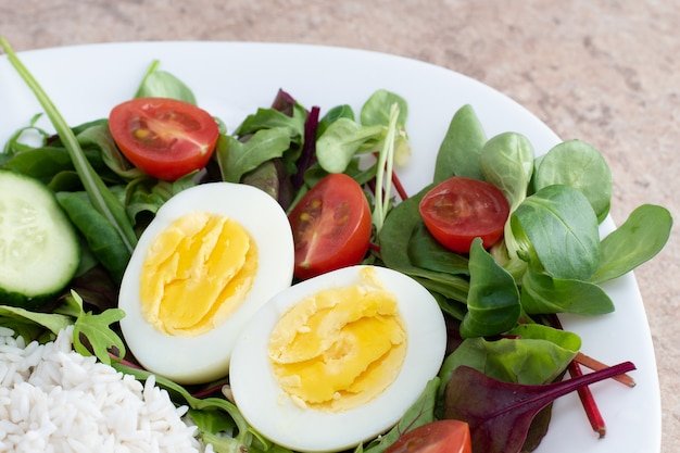 Salad of green vegetables, tomato and rice in a white plate. Rice with vegetables and eggs on a white plate.