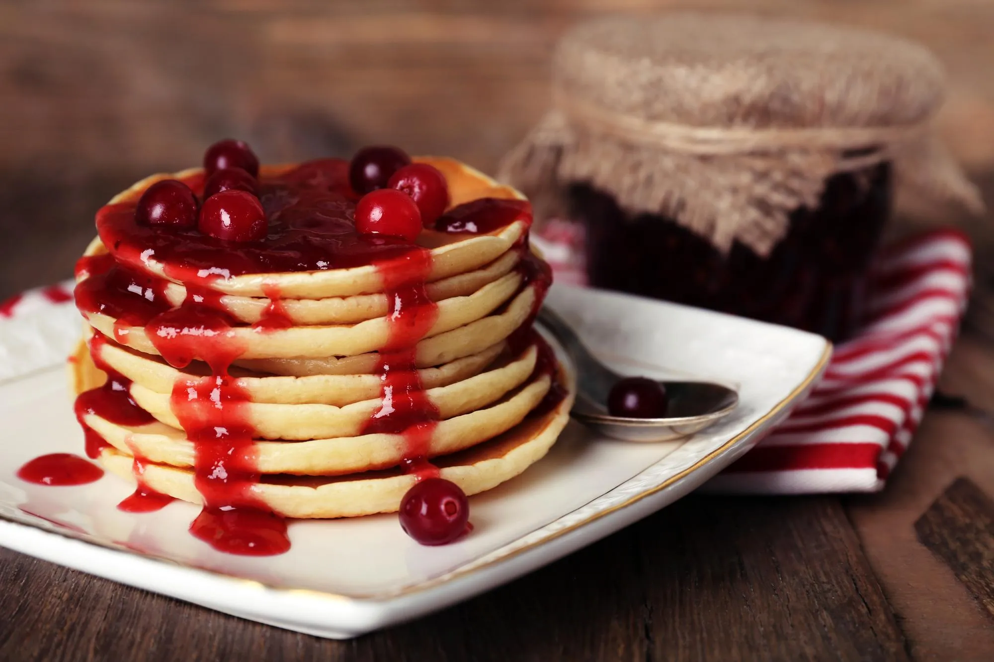 Stack of delicious pancakes with cranberries and jam on plate and napkin on wooden background