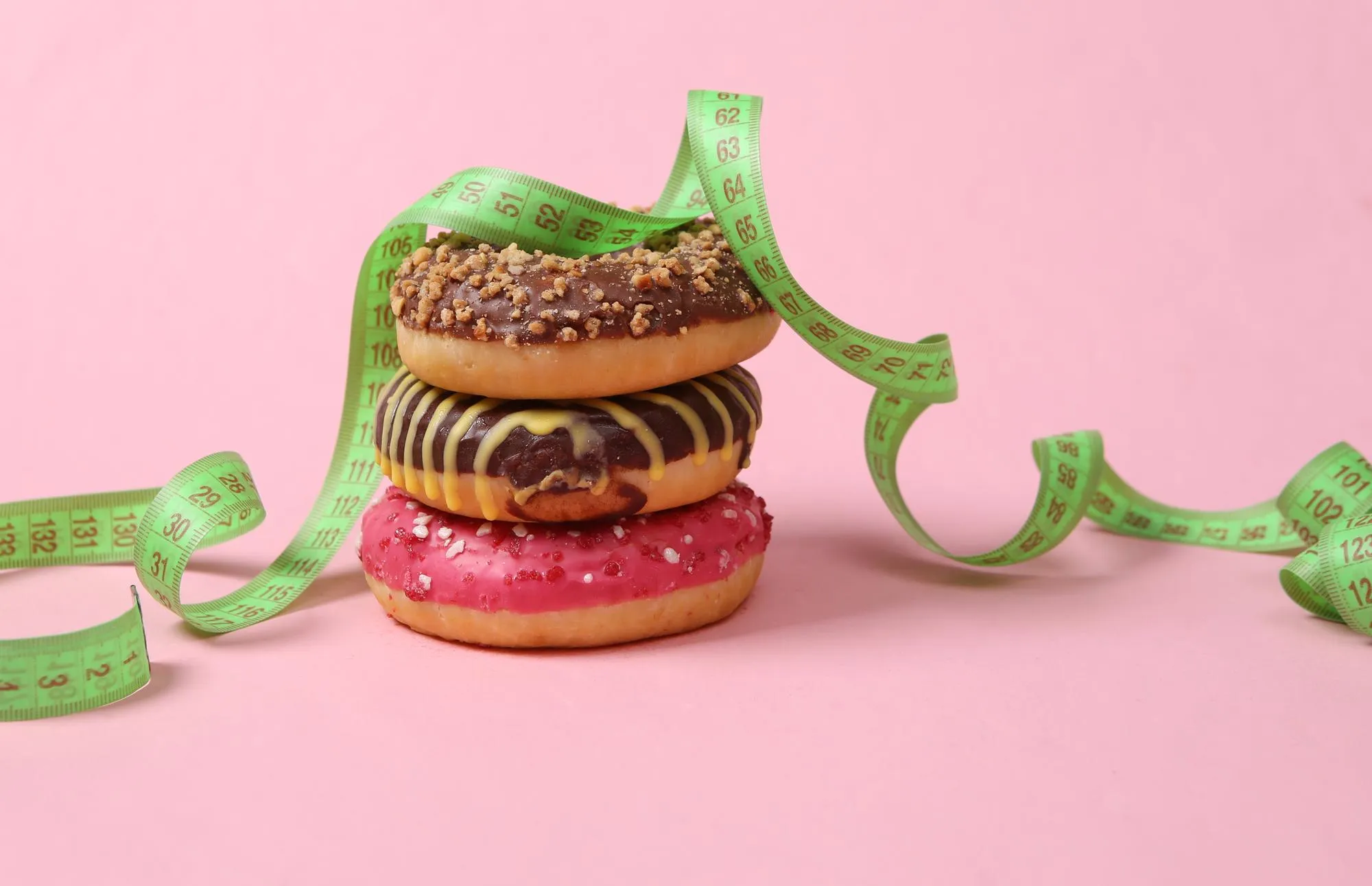 A stack of donuts with a measuring tape on a pink background Diet concept