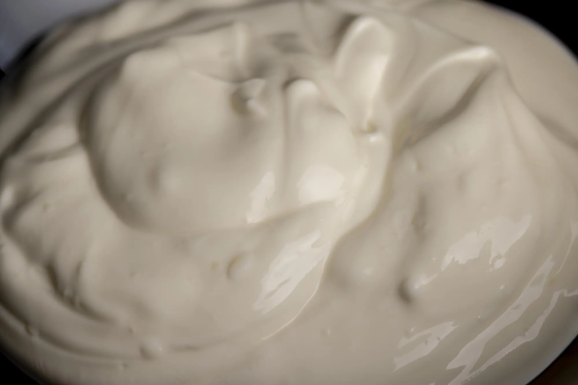 White fresh sour cream in a black glass plate fresh sour cream from cow's milk poured into a glass plate