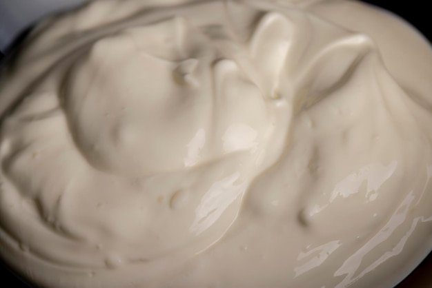 White fresh sour cream in a black glass plate fresh sour cream from cow's milk poured into a glass plate