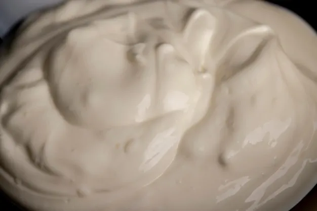 White fresh sour cream in a black glass plate fresh sour cream from cow's milk poured into a glass plate