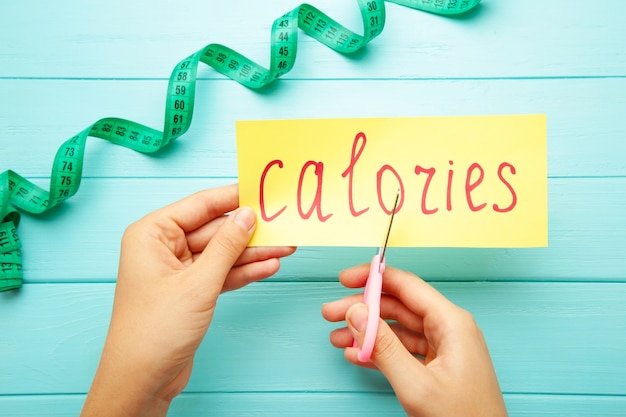Woman hand holding card with the word calories. Cutting calories. Top view