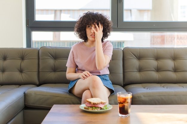 Young pretty woman having a sandwich sitting on a sofa at home
