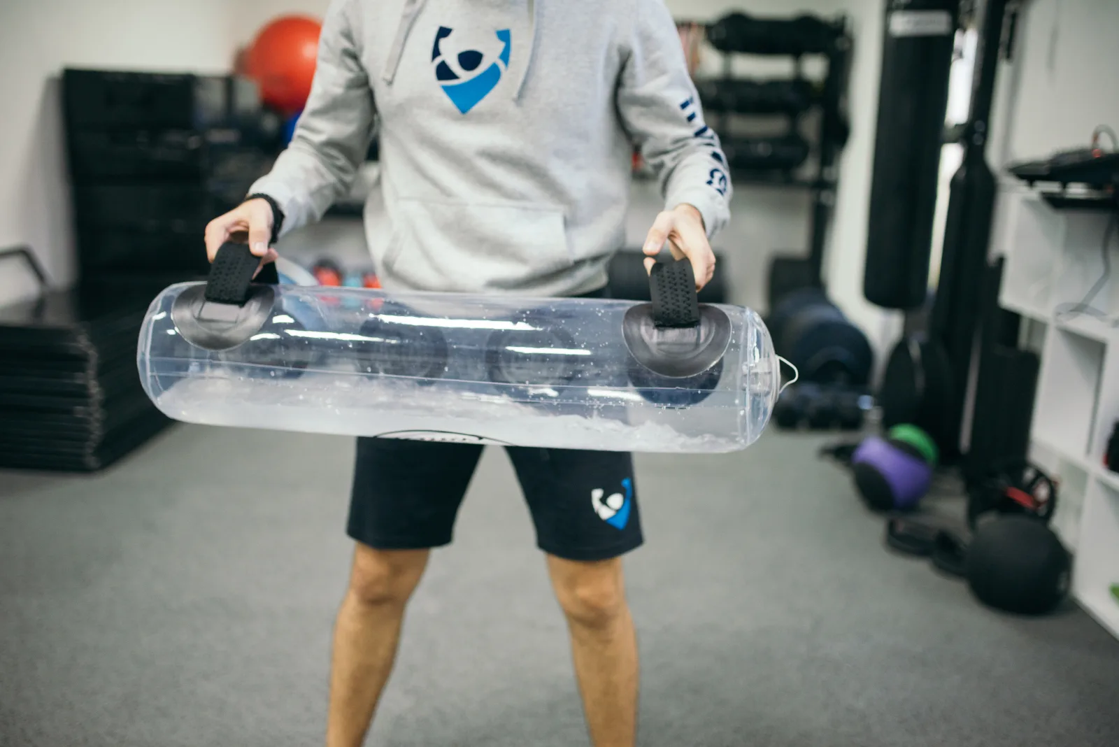 A person is actively using a transparent training device designed for strength exercises in a gym setting. The individual demonstrates proper handling techniques with a focus on fitness improvement.